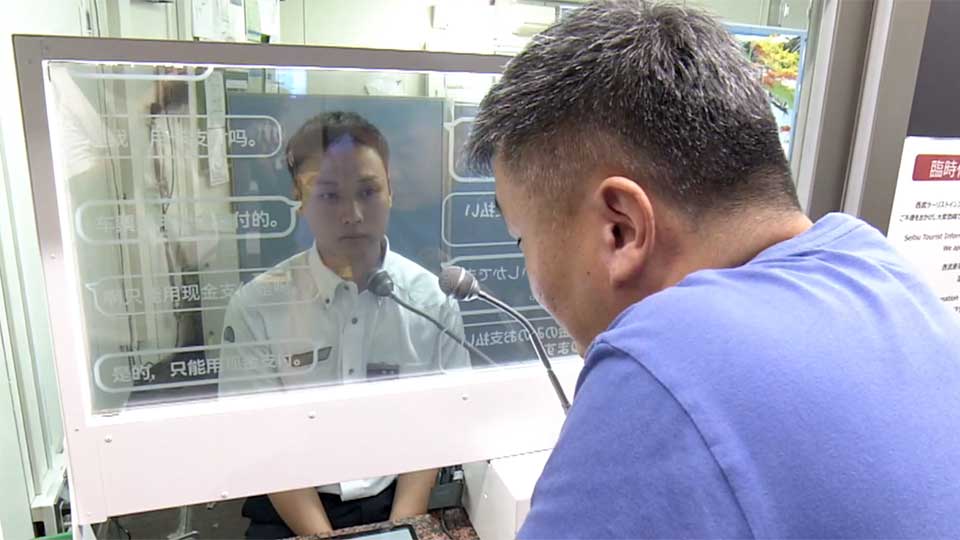 Một du khách từ Trung Quốc dùng máy phiên dịch để giao tiếp với nhân viên nhà ga về cách mua vé.